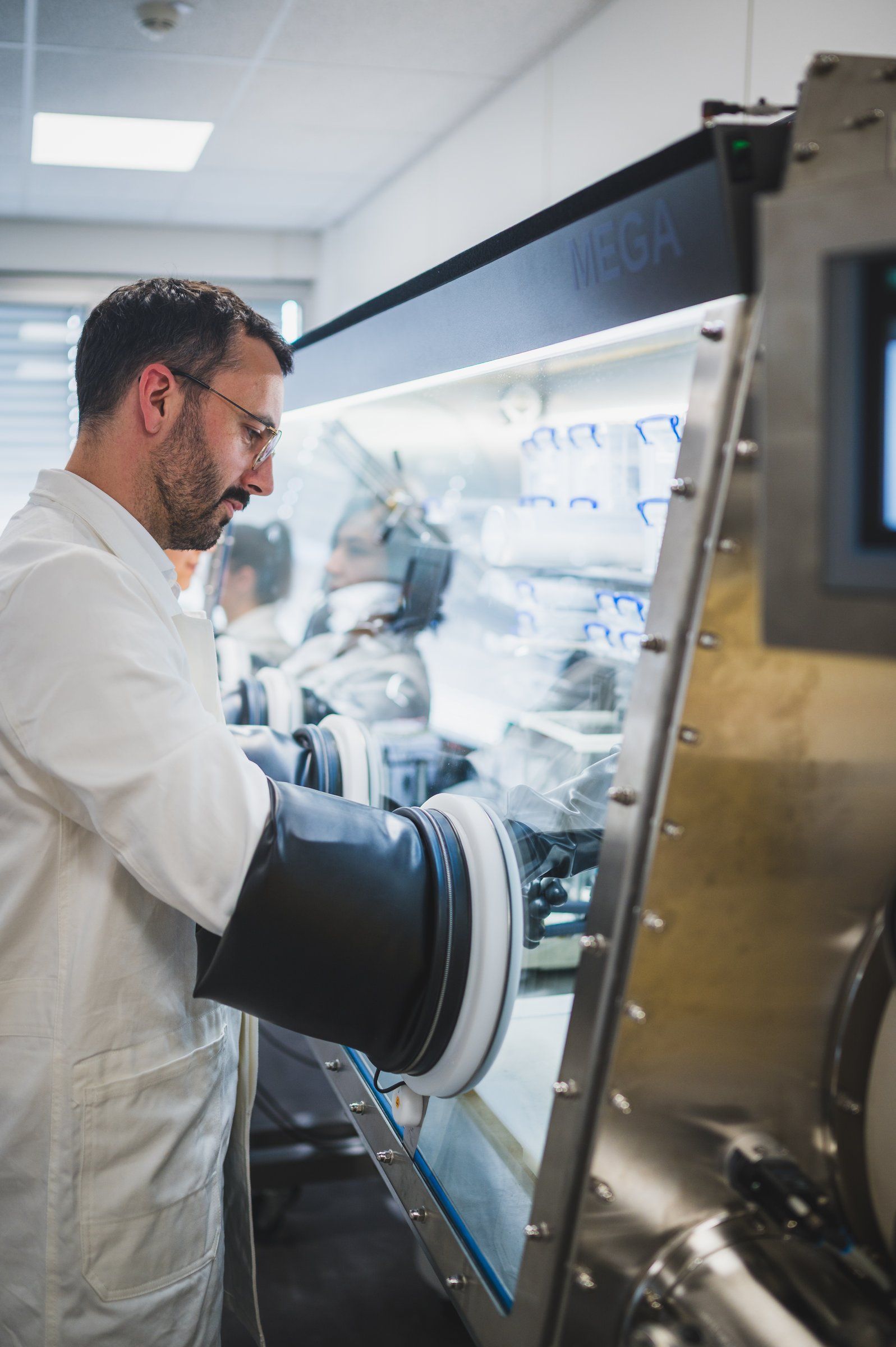 Hands in the gauntlets of a glovebox, handling a cell under argon