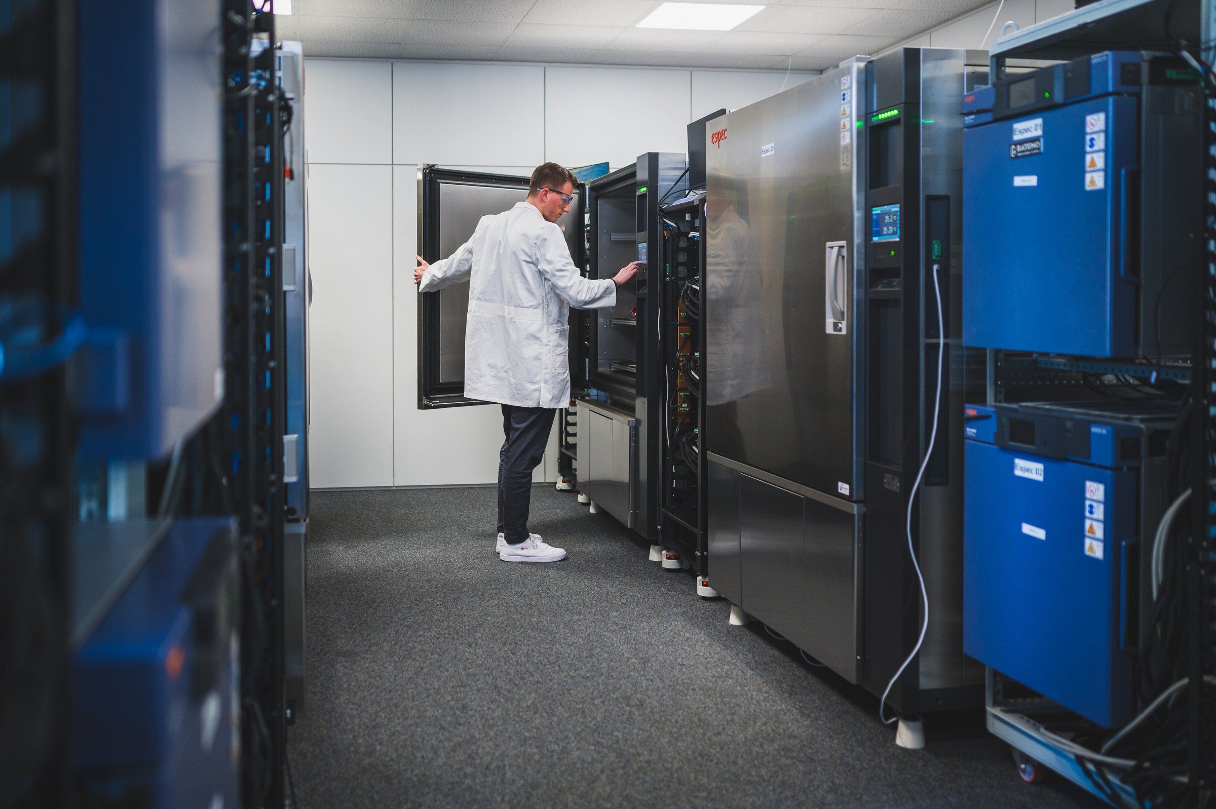 Batemo engineer opening a climate chamber in the test field, flanked by a corridor of cycler cabinets